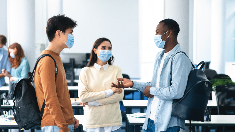 Three students in masks talking to one another