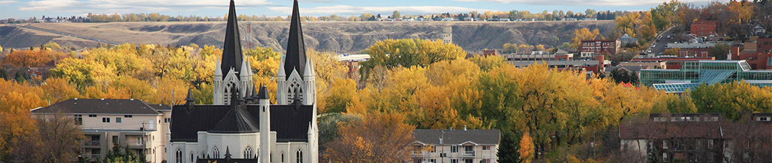 Black and white church in front of a grove of fall trees.