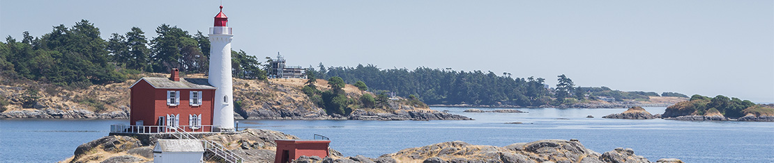 White and red lighthouse on a small rock island in a body of water.