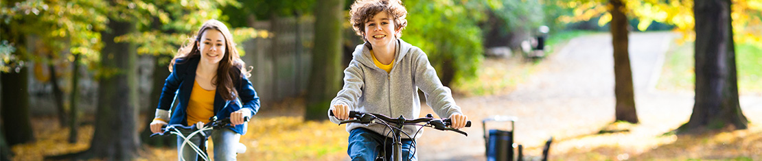 Two kids riding their bikes in a leaf-strewn park